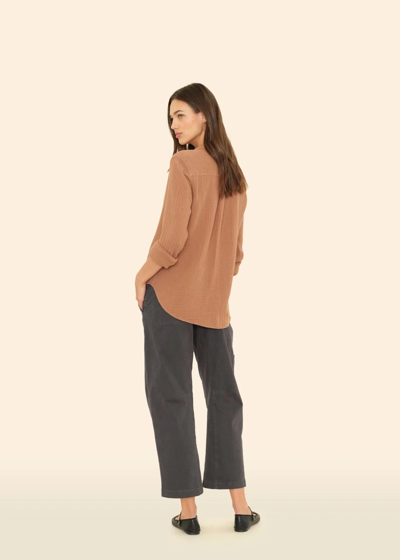 Woman wearing a brown blouse and gray pants on a beige background