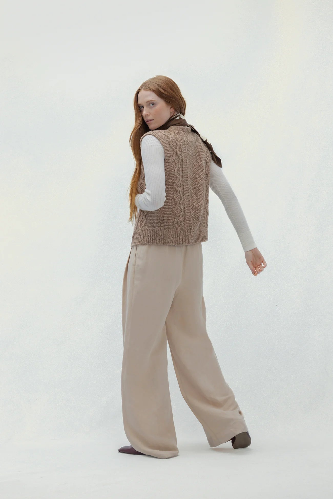 Woman wearing a brown vest and beige pants on a white background
