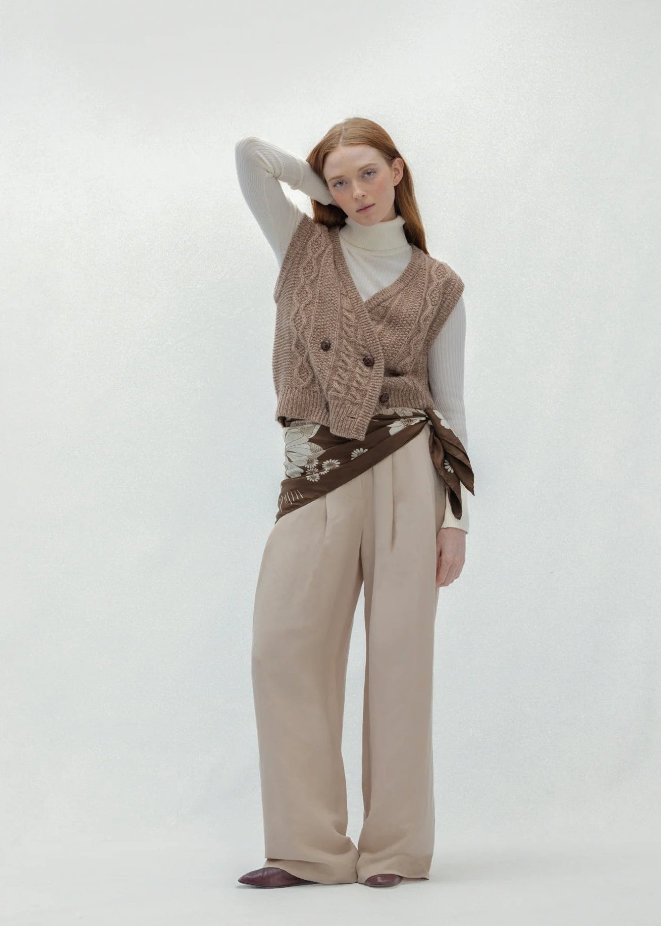Woman wearing a brown knitted vest and scarf on a white background