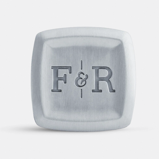 A square metallic accessory with rounded corners, featuring the engraved initials 'F&R' in the center, shown on a clean light gray background.