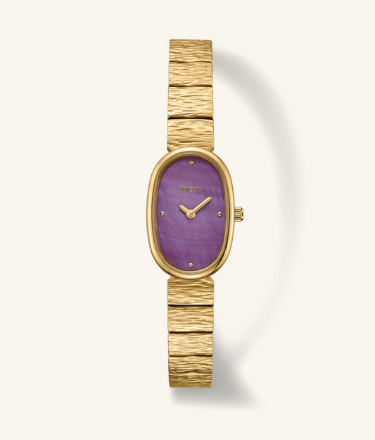 A women's wristwatch with a textured gold-tone metal link bracelet, an oval bezel, and a purple dial with gold-tone hands and markers.
