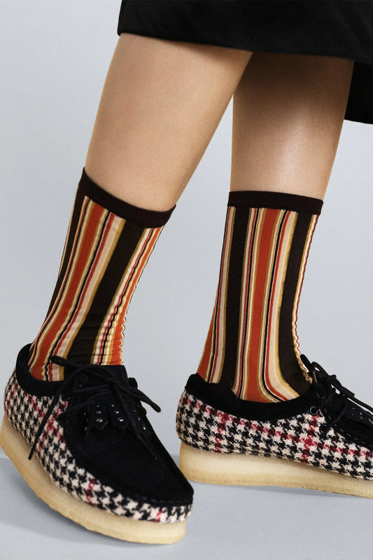 Person wearing striped socks and houndstooth shoes on a light gray background