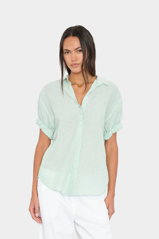 Woman wearing a light green stripe shirt and white pants on a plain background 